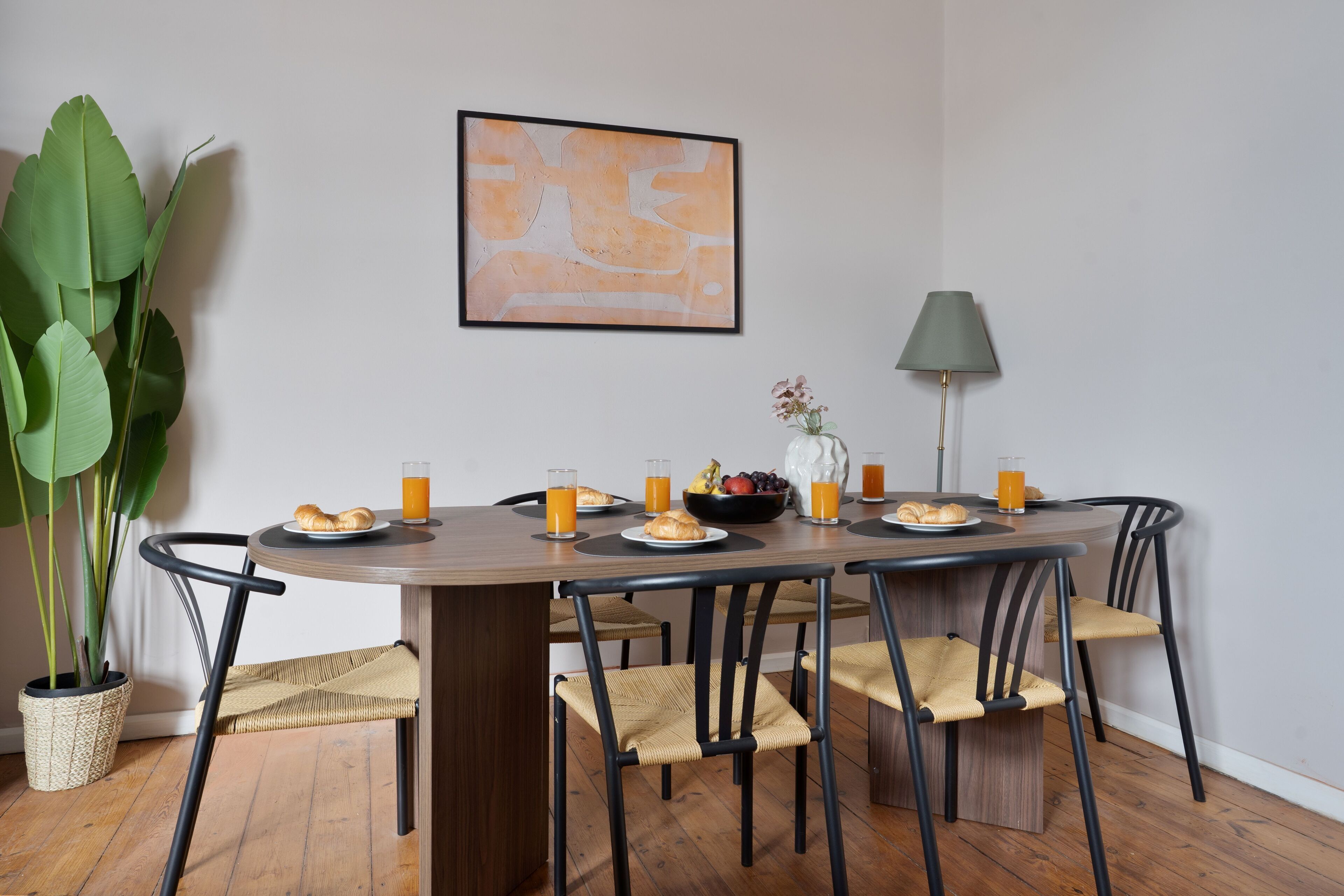 A dining area with a wooden table, black chairs, and a potted plant.