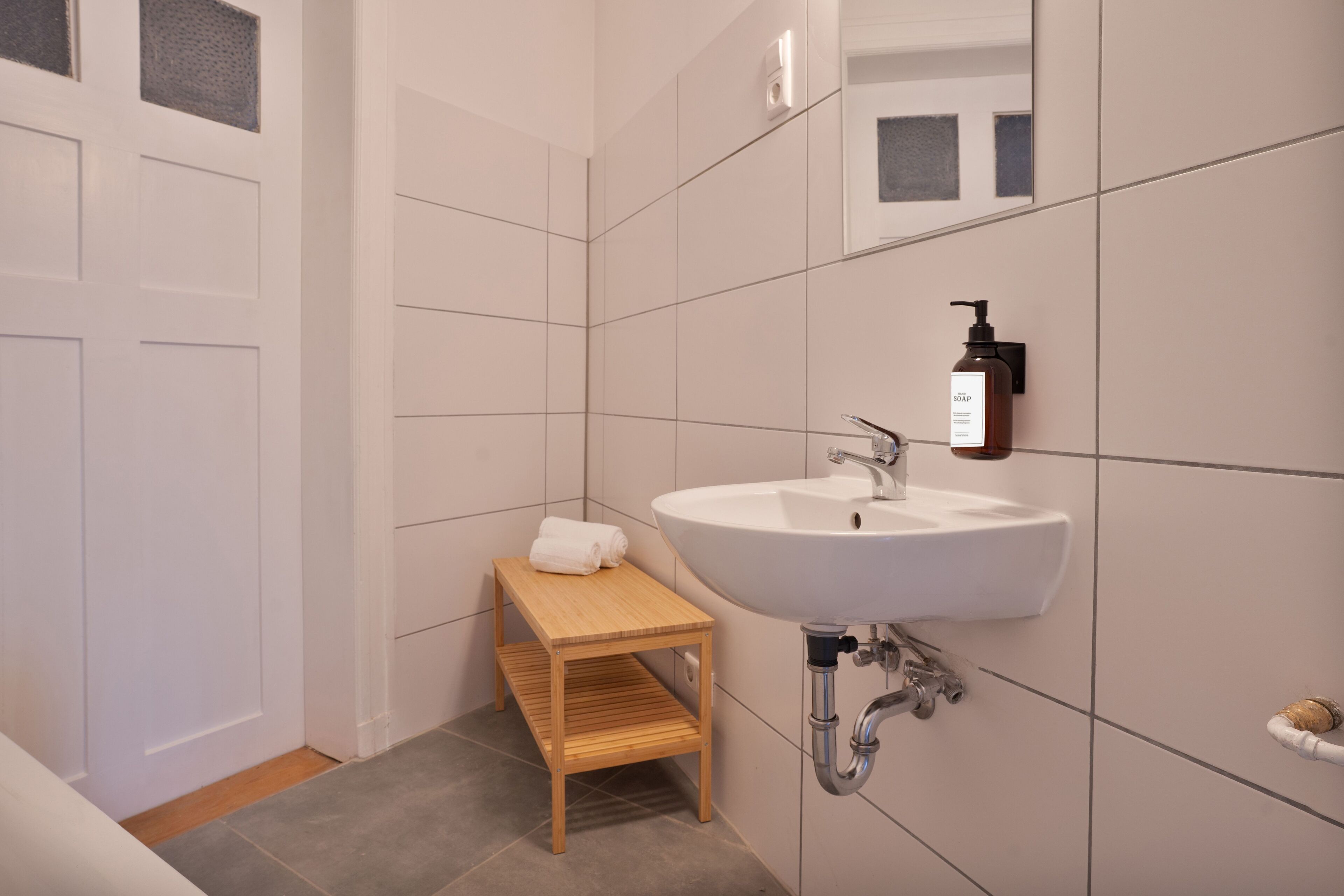 A modern bathroom with a white sink, wooden shelf, and a towel rack.
