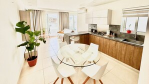 A modern kitchen with a dining area, featuring a glass table and chairs, a potted plant, and a view of the city. - Santa Venera - The Papillon Penthouse (L-Imsida)