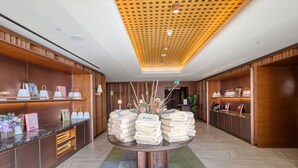 Un'accogliente hall d'hotel con pannelli in legno, un tavolo rotondo centrale con asciugamani piegati e un soffitto decorato con un motivo geometrico.
