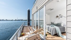 Un balcon avec vue sur l’eau, un lit avec vue et une petite table avec des fruits.
