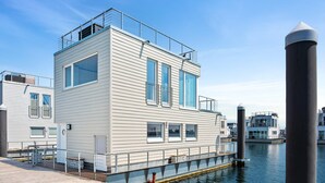 Un bâtiment moderne situé au bord de l’eau, doté de grandes fenêtres, d’une terrasse et d’un quai s’avançant dans l’eau.