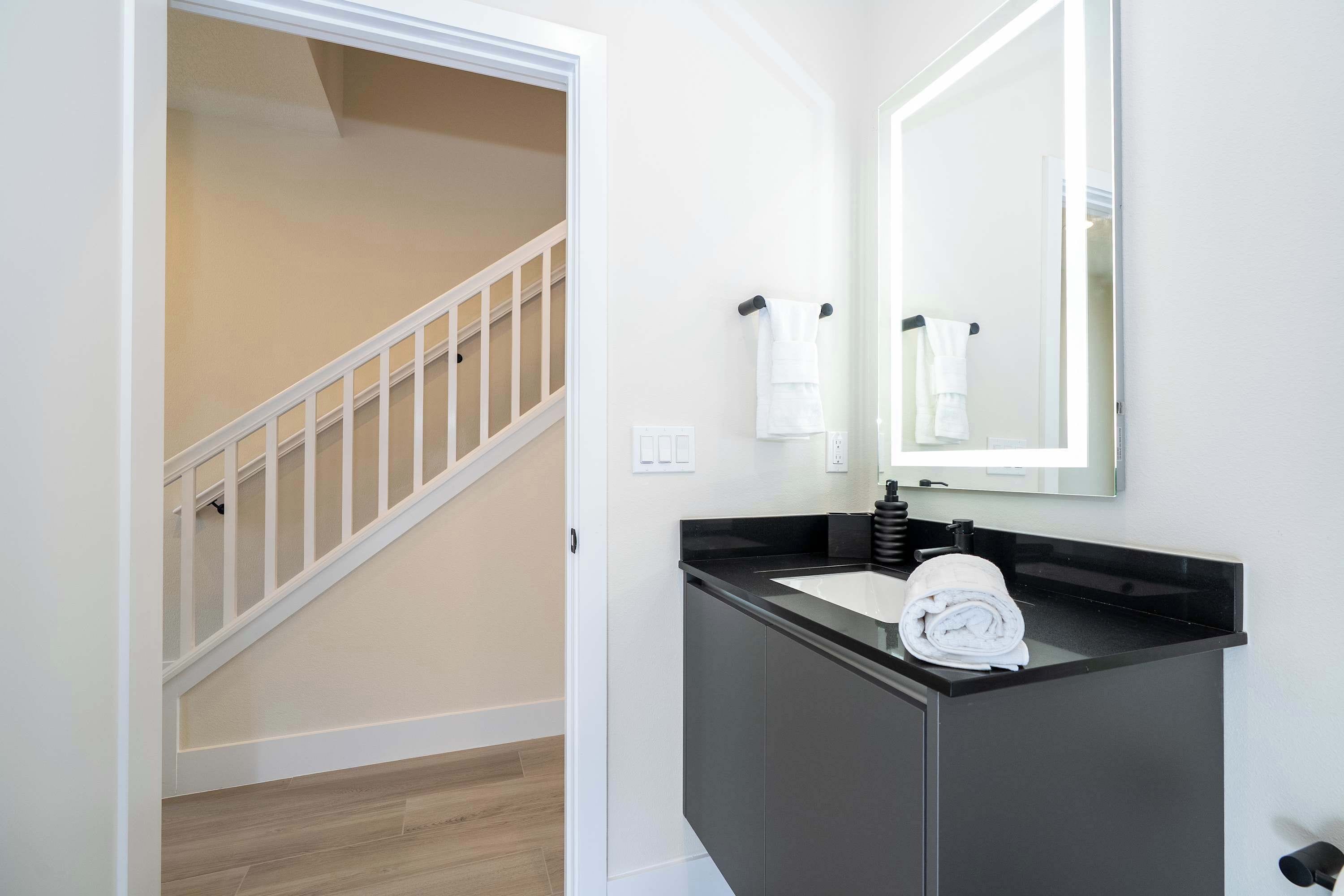 A modern bathroom with a black sink, a large mirror, and a white towel hanging on the wall.