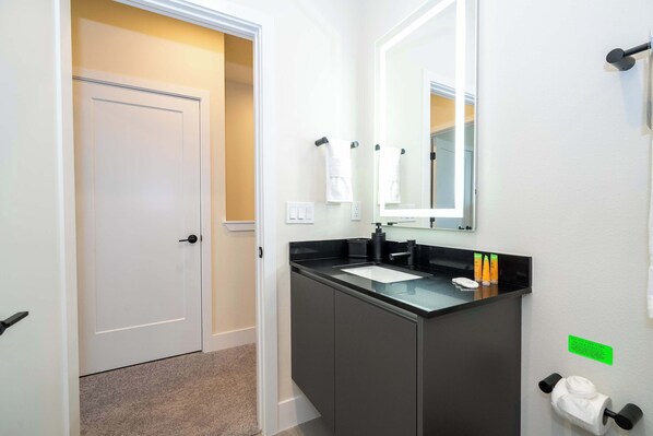 A modern bathroom with a white door, a black sink, and a mirror.