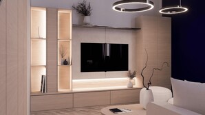 Un salon moderne avec un téléviseur à écran plat fixé au mur, un canapé, une table basse et une bibliothèque intégrée agrémentée d’objets décoratifs.
