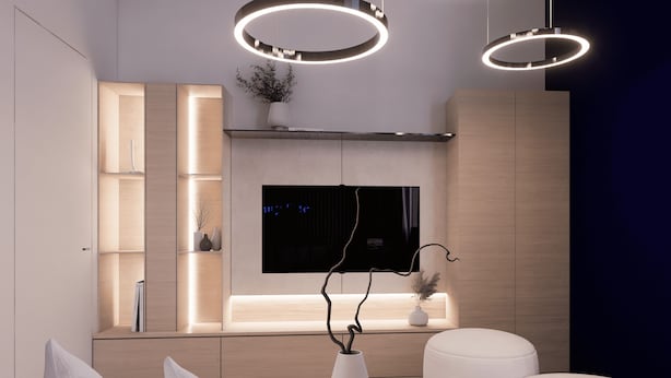 Un salon moderne avec un téléviseur, un vase blanc orné de branches et des luminaires circulaires au plafond.