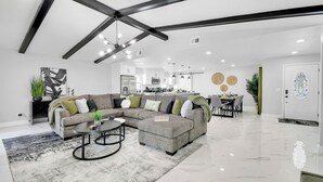 Un salon moderne avec un canapé d’angle, une table basse et un coin repas agrémenté d’un lustre.