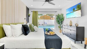 Une chambre moderne avec un lit, un ventilateur de plafond, une télévision et une vue sur une piscine.