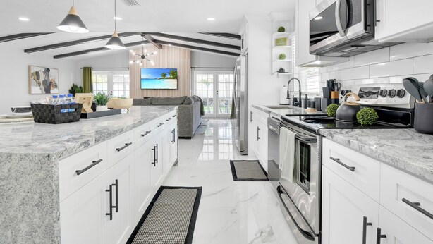 Une cuisine moderne avec des meubles blancs, un grand îlot central, des appareils en acier inoxydable et des luminaires suspendus.