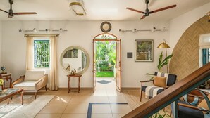 A spacious living room with a large window, a round mirror, a wooden coffee table, and a sofa. There is a staircase leading to another level. - Sanctuary by RÊVE Escapes (Siolim)