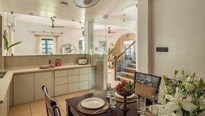 A modern kitchen with a dining area, a staircase, and a view of the outside. - Sanctuary by RÊVE Escapes (Siolim)