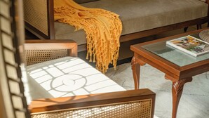 A room with a sofa, a wooden coffee table with a magazine, and a chair with a woven backrest. - Sanctuary by RÊVE Escapes (Siolim)