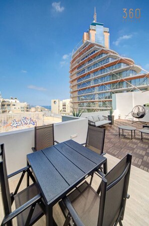 A rooftop terrace with outdoor seating and a view of a modern building.