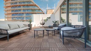 Una terraza en la azotea con un área de estar moderna al aire libre, que incluye un sofá y sillones, y vistas a un edificio distintivo al fondo.