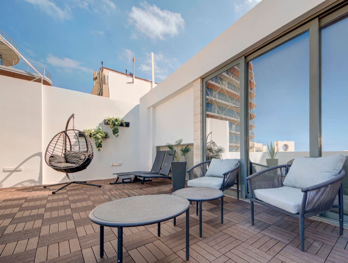 A rooftop terrace with a hanging chair, lounge chairs, and a table.