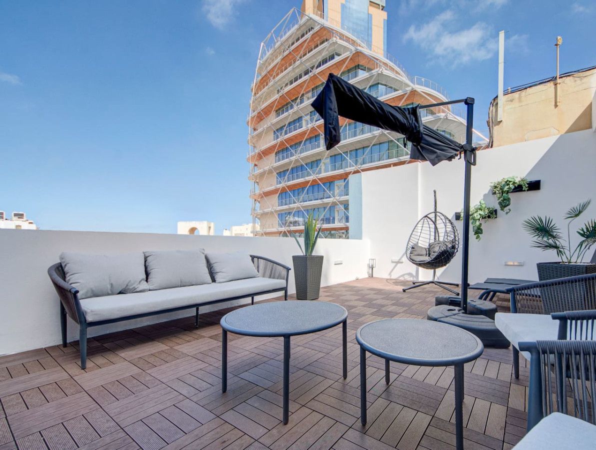Terraza en la azotea con sofá, mesas redondas y una silla colgante.