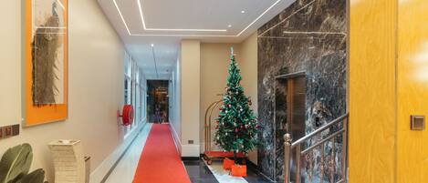 A hotel corridor with a red carpet, a Christmas tree, marble walls, and a staircase.