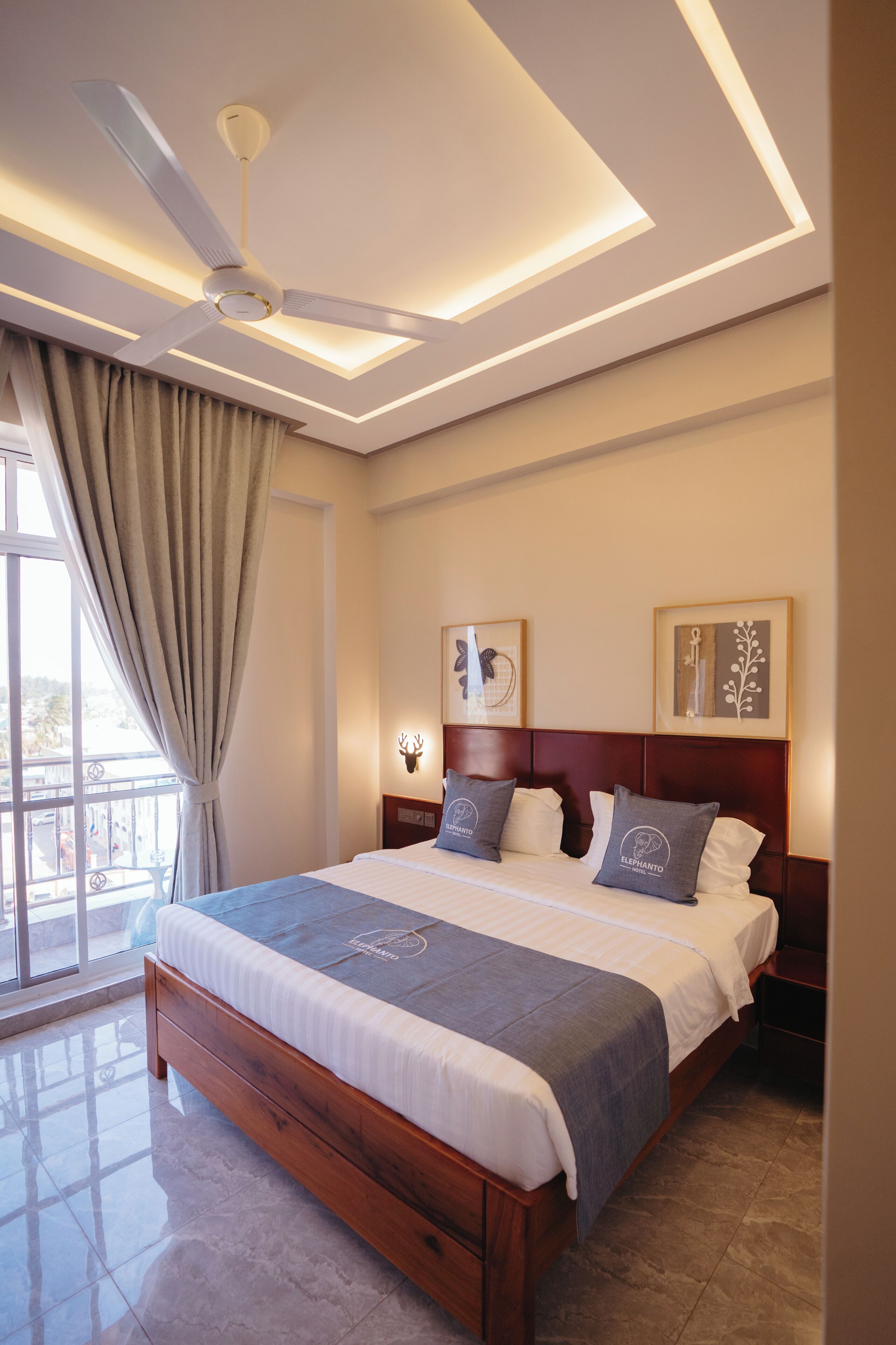 A modern hotel room with a large bed, ceiling fan, and artwork on the walls.