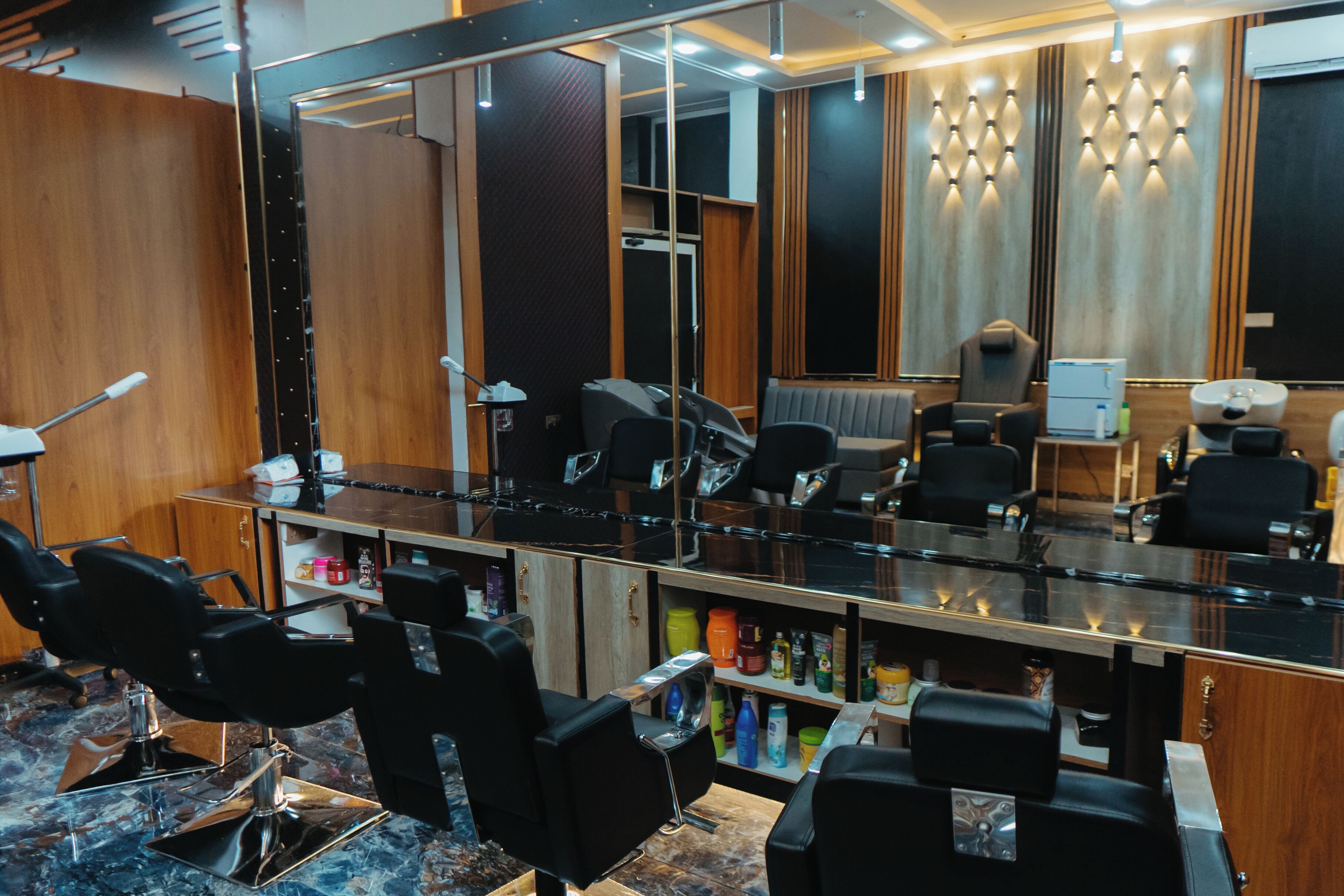 A salon with multiple black salon chairs, a large mirror, and shelves with various hair products.