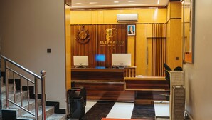 A hotel reception area with a wooden reception desk, a clock, and a framed photo on the wall. - Elephantohotel (Zanzibar Town)