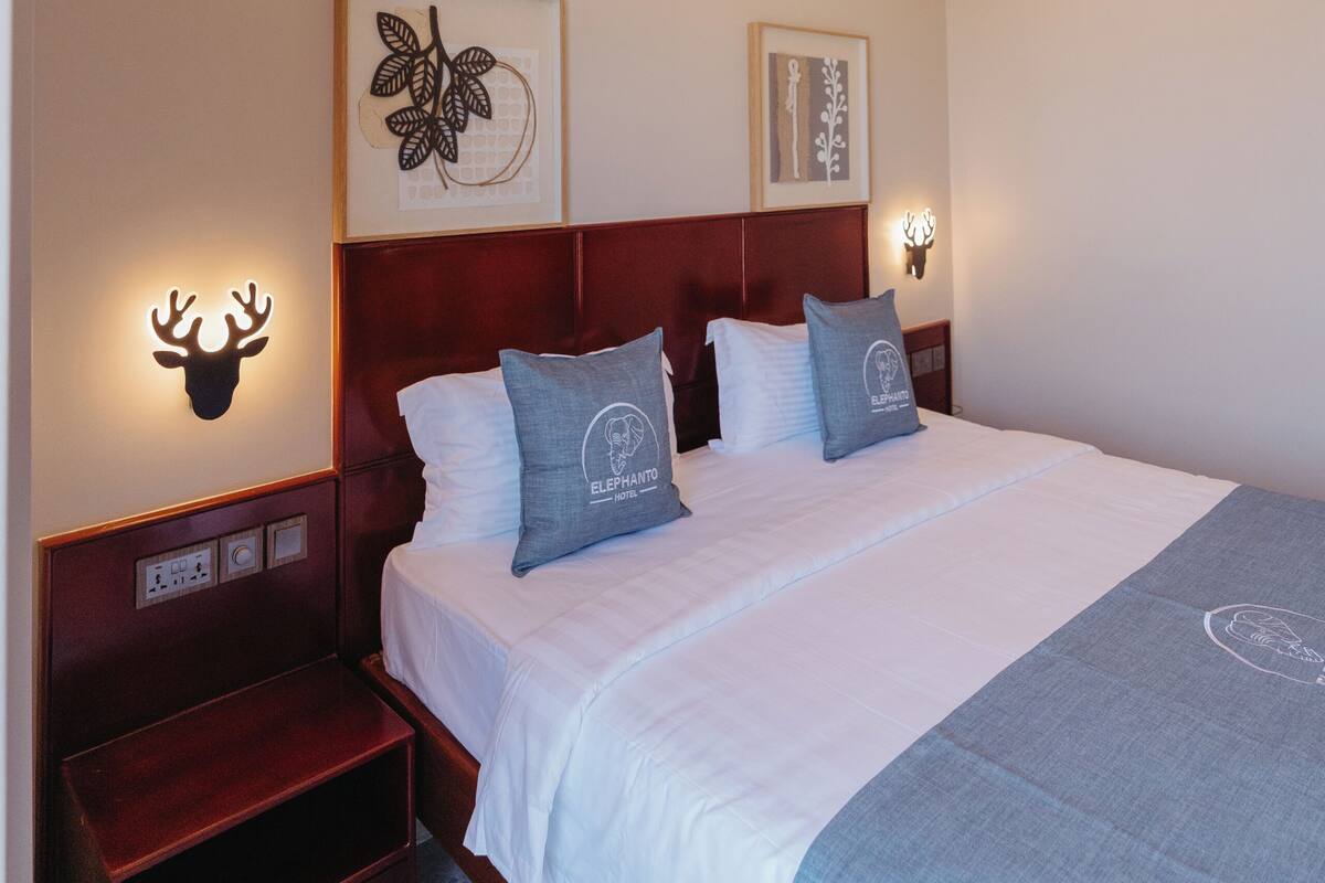 Habitación de hotel con cama, mesitas de noche, lámparas de pared e ilustraciones enmarcadas.