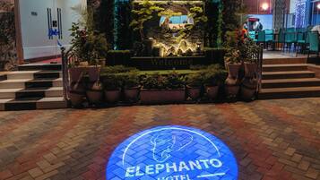 Entrada del Hotel Elephantto Zanzibar con un cartel de bienvenida, plantas en macetas y un logo azul iluminado en el suelo.