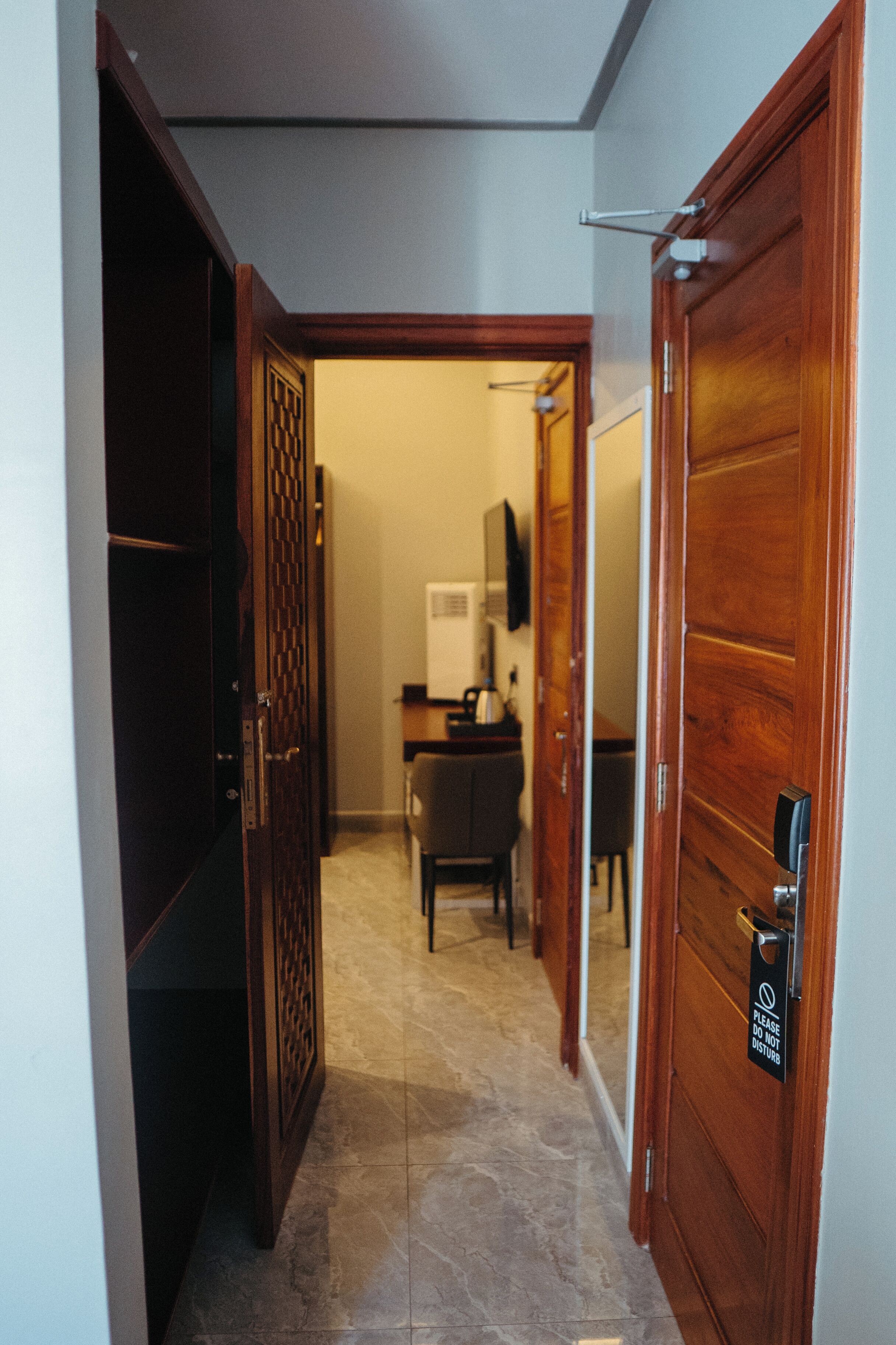 Un pasillo con puertas de madera, suelo de baldosas y un escritorio con una silla al fondo.