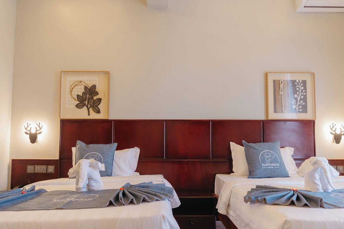 Habitación de hotel con dos camas, cabecero de madera, una obra de arte enmarcada en la pared y una decoración de cabeza de ciervo fijada a la pared.