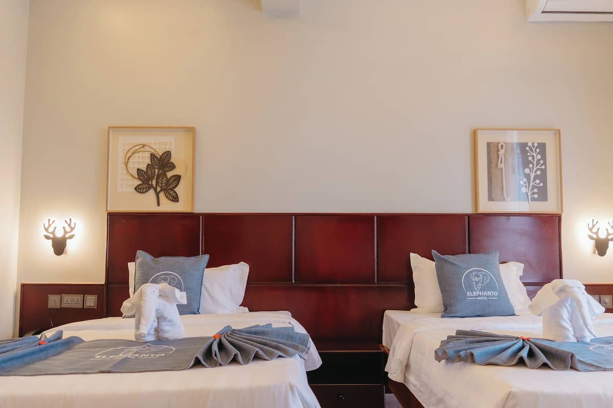 A hotel room with two beds, a wooden headboard, a framed artwork on the wall, and a wall-mounted deer head decoration.