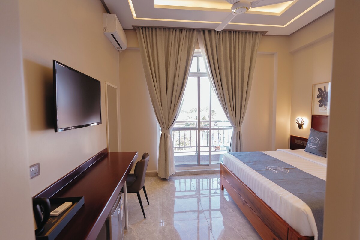A hotel room with a bed, a desk, a chair, a TV, and a window with curtains.