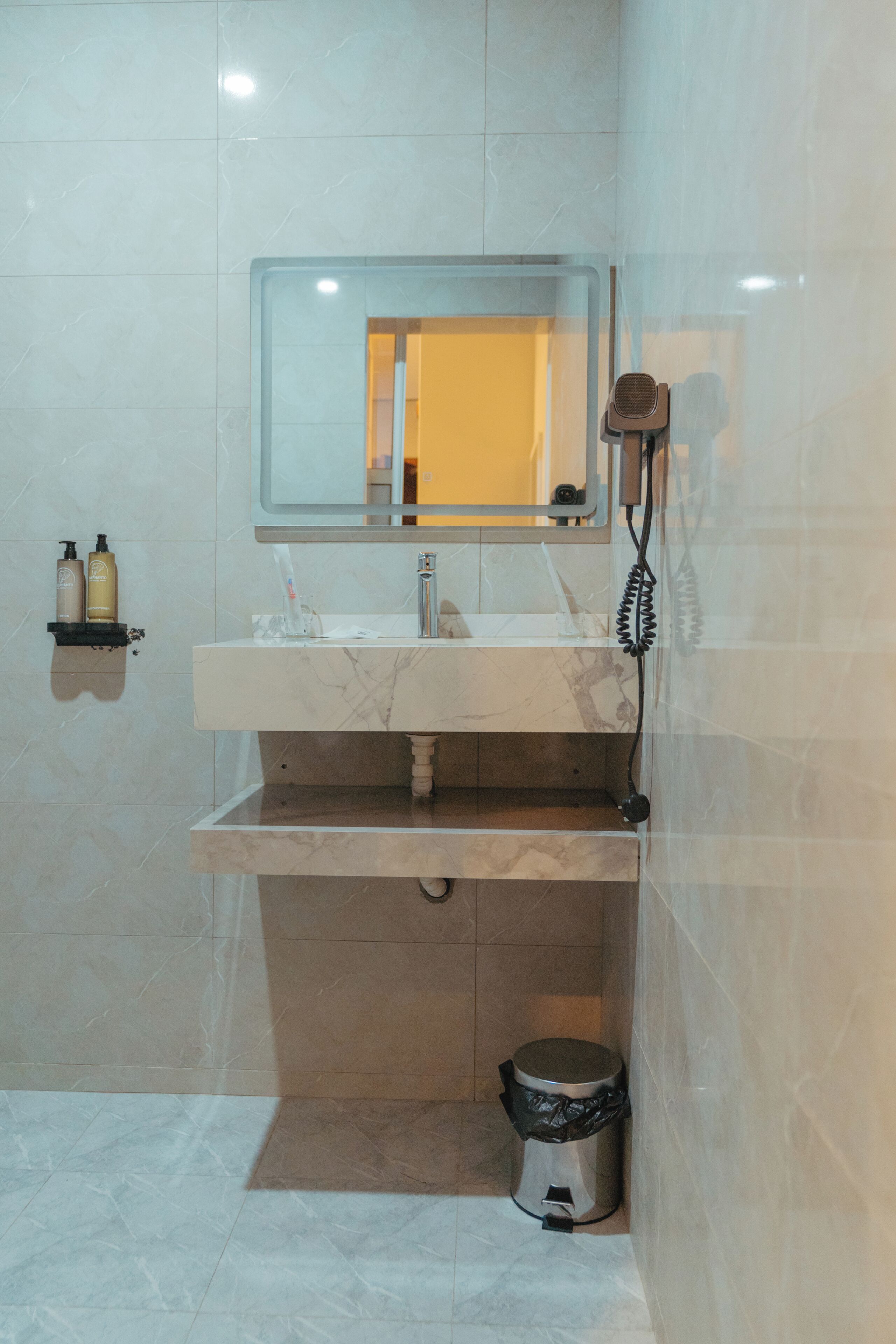 A bathroom with a marble sink, a mirror, a handheld showerhead, and a trash bin.