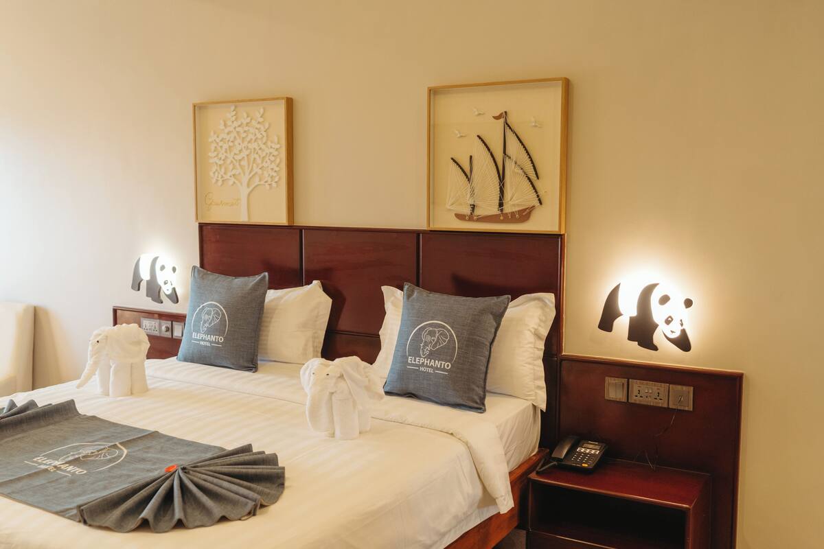 Una habitación de hotel con cama, almohadas, mesita de noche y un teléfono, además de decoración en la pared.