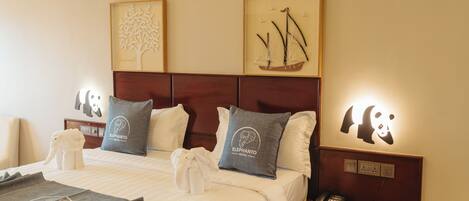Una habitación de hotel con cama, almohadas, mesita de noche y un teléfono, además de decoración en la pared.