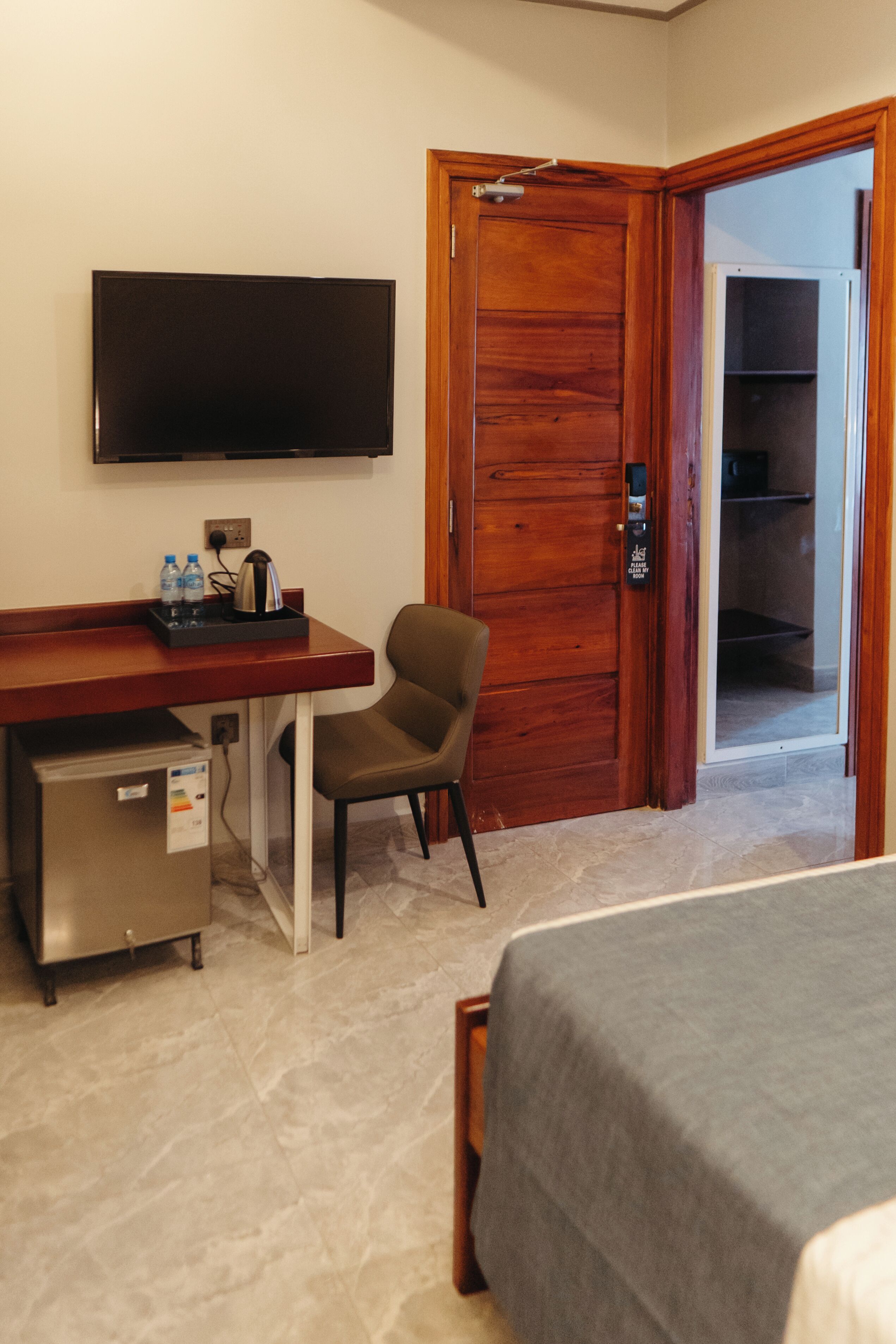 Habitación de hotel con cama, escritorio, televisor de pantalla plana, silla, refrigerador pequeño y puerta de madera.