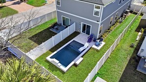 A modern two-story house with a rectangular swimming pool, a covered patio, and a fenced yard.