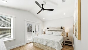 A bedroom with a bed, bedside tables, a ceiling fan, and a large window with blinds.
