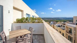 Un balcon avec une table et des chaises, offrant une vue sur le paysage urbain et les collines lointaines.