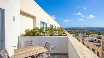 A balcony with a table and chairs, overlooking a cityscape and distant hills.