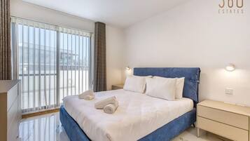 Una habitación de hotel moderna con una cama grande, una mesita de noche y un ventanal con cortinas.