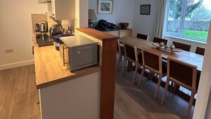 Une cuisine moderne avec un plan de travail en bois, un coin repas comprenant une table et des chaises, et une vue sur un jardin par le biais d’une fenêtre.
