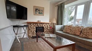 Un salon doté d’une cheminée en pierre, d’un téléviseur à écran plat fixé au mur, d’une table basse en verre et d’un canapé agrémenté de coussins à motifs.