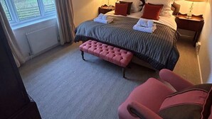 Une chambre à coucher avec un lit, des tables de chevet, un banc, une chaise et une fenêtre.