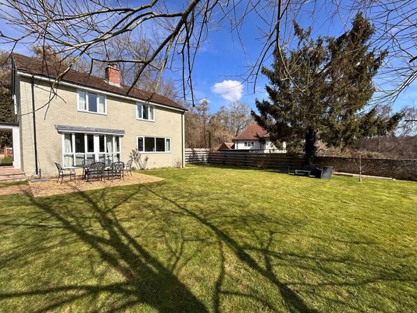 A house with a well-maintained lawn, a patio with outdoor furniture, and a large tree in the yard.