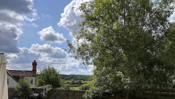 Une terrasse avec une table et des chaises, un mur en pierre et un grand arbre.