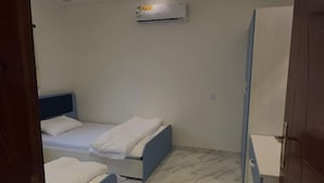 A modern bedroom with two beds, a built-in wardrobe, and an air conditioning unit. - Al-Mutawa Residential Countryside Resort (Al Mandaq)