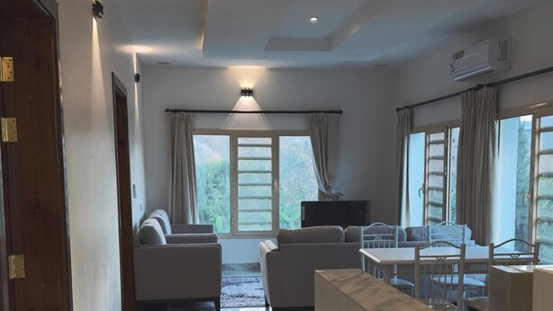 A spacious living area with a marble floor, a sofa set, a dining table with chairs, and large windows with curtains. - Al-Mutawa Residential Countryside Resort (Al Mandaq)