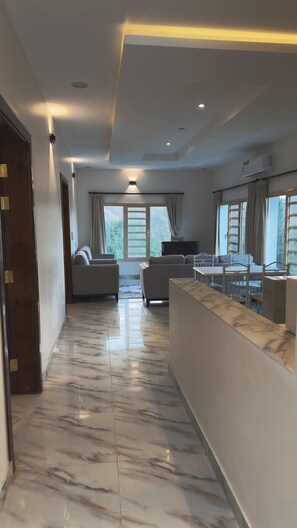 A spacious living area with a marble floor, a sofa set, a dining table with chairs, and large windows with curtains. - Al-Mutawa Residential Countryside Resort (Al Mandaq)