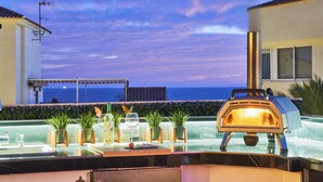 Una terrazza sul tetto con forno a legna, piante in vaso e vista sull'oceano.