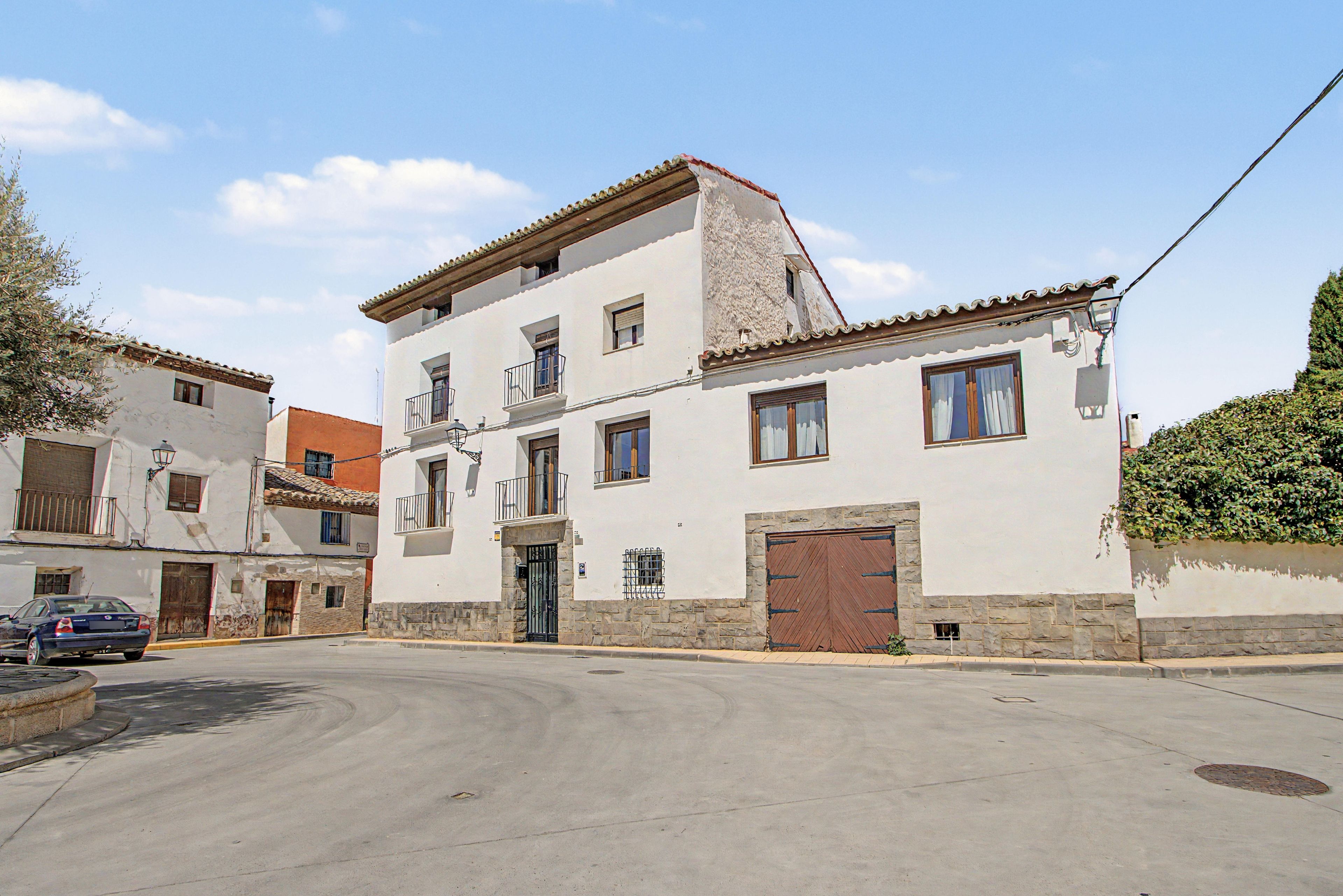 Un edificio de dos pisos con fachada de piedra, una entrada central con puerta de madera y un pequeño balcón en el segundo nivel.