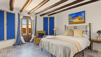 A hotel room with a bed, a chair, a desk, and a painting on the wall.